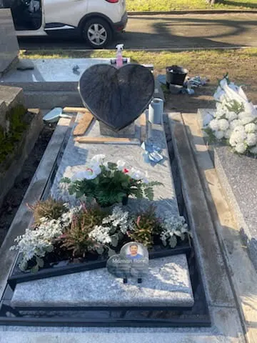 Vue d’une sépulture avec une plaque en forme de cœur, des fleurs et des ornements sur la dalle.